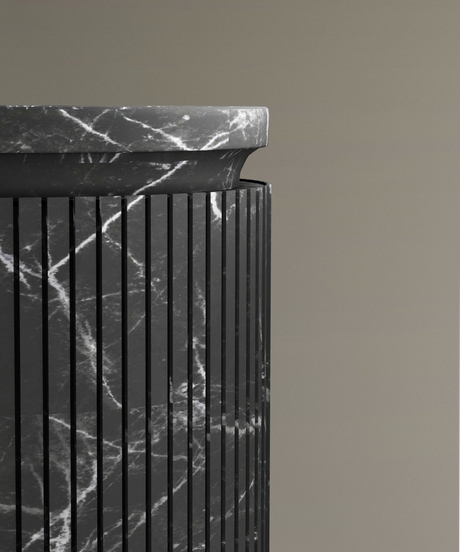 Close-up of a black marble pedestal with vertical grooves and white veining, topped with a matching marble slab against a plain taupe background.