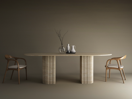 The TRAVERTABLE Oval Travertine Dining Table features a fluted round solid stone base and customizable options. Positioned between wooden chairs with white cushions, it displays minimalist vases and a branch on its heirloom-quality surface.