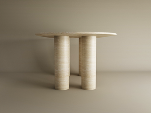 The TRAVERTABLE Oval Travertine Dining Table features a pure travertine stone tabletop and sturdy cylindrical base, offering customizable options and heirloom quality for timeless appeal against a neutral backdrop.