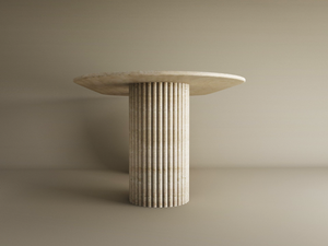 The TRAVERTABLE Oval Travertine Dining Table features a customizable organic stone top and a vertical groove base, set against a plain beige background.