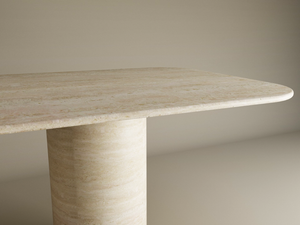 A close-up of the TRAVERTABLE Rectangular Travertine Dining Table, featuring a smooth cylindrical pure travertine stone base and rounded edges, showcases its heirloom-quality customizable tabletop against a light background.